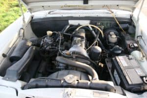 Geöffnete Motorhaube eines Oldtimers, während ein Kfz-Gutachter den Motor auf Zustand, Originalität und Wert überprüft.