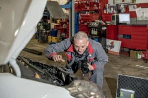 Ein Kfz-Gutachter fotografiert einen Oldtimer mit offener Motorhaube, um den Fortschritt der Restaurierung fachgerecht zu dokumentieren.