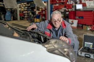 Der Kfz-Gutachter arbeitet am geöffneten Motor eines Fahrzeugs und überprüft technische Komponenten auf Schäden und Funktionstüchtigkeit.