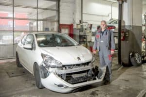 Ein Kfz-Gutachter begutachtet in einer Werkstatt ein Fahrzeug mit Totalschaden und erstellt ein professionelles Gutachten zur Schadenshöhe.