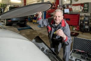 Ein Kfz-Gutachter leuchtet mit einer Taschenlampe in den Motorraum, um den Zustand und mögliche Schäden zu überprüfen.