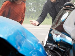 Zwei Unfallbeteiligte stehen an stark beschädigten Autos und klären den Unfallhergang nach einer Kollision