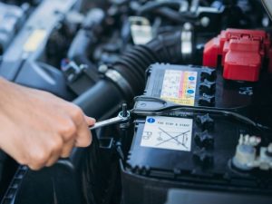 Hand löst die Autobatterie im Motorraum als Motiv für Batteriewechsel und technische Fahrzeugprüfung